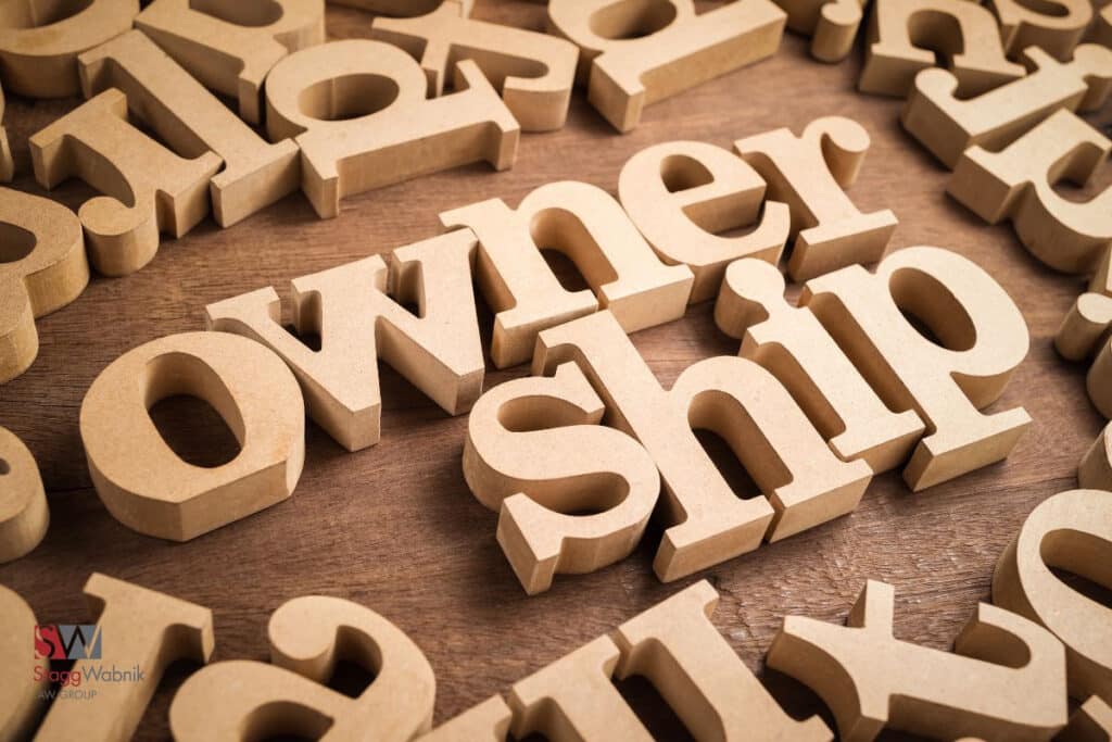 Wooden letters spelling "ownership" on a wooden surface, surrounded by scattered letters. A logo with "SW Stagg Wabnik AW Group" is visible.