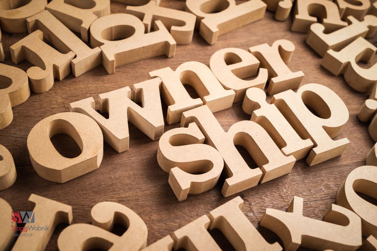 Wooden letters spelling "ownership" on a wooden surface, surrounded by scattered letters. A logo with "SW Stagg Wabnik AW Group" is visible.