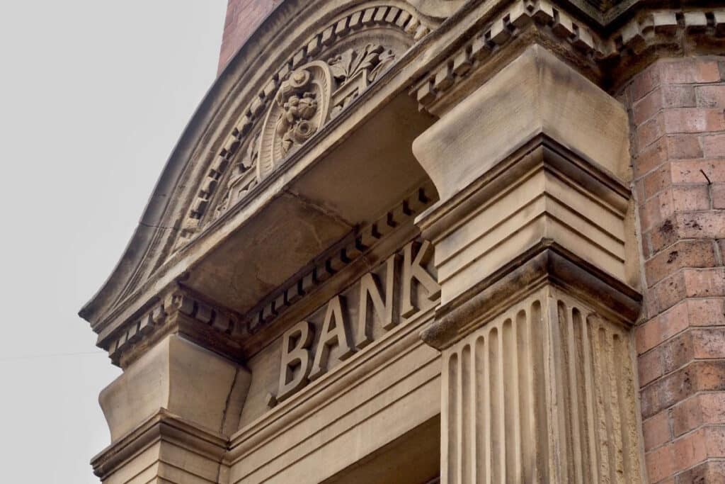 Ornate stone bank facade with the word "BANK" inscribed. Features column details and a decorative arch. Calm, historical ambiance.
