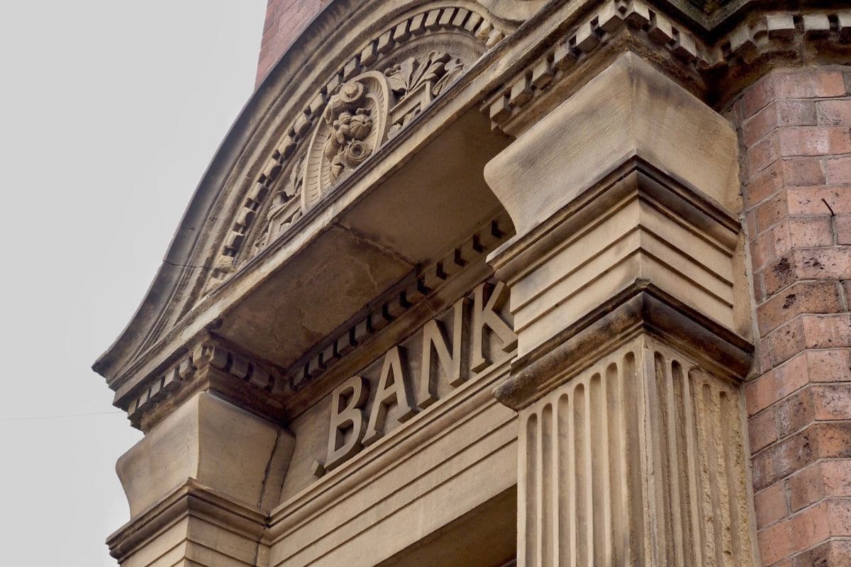 Ornate stone bank facade with the word "BANK" inscribed. Features column details and a decorative arch. Calm, historical ambiance.