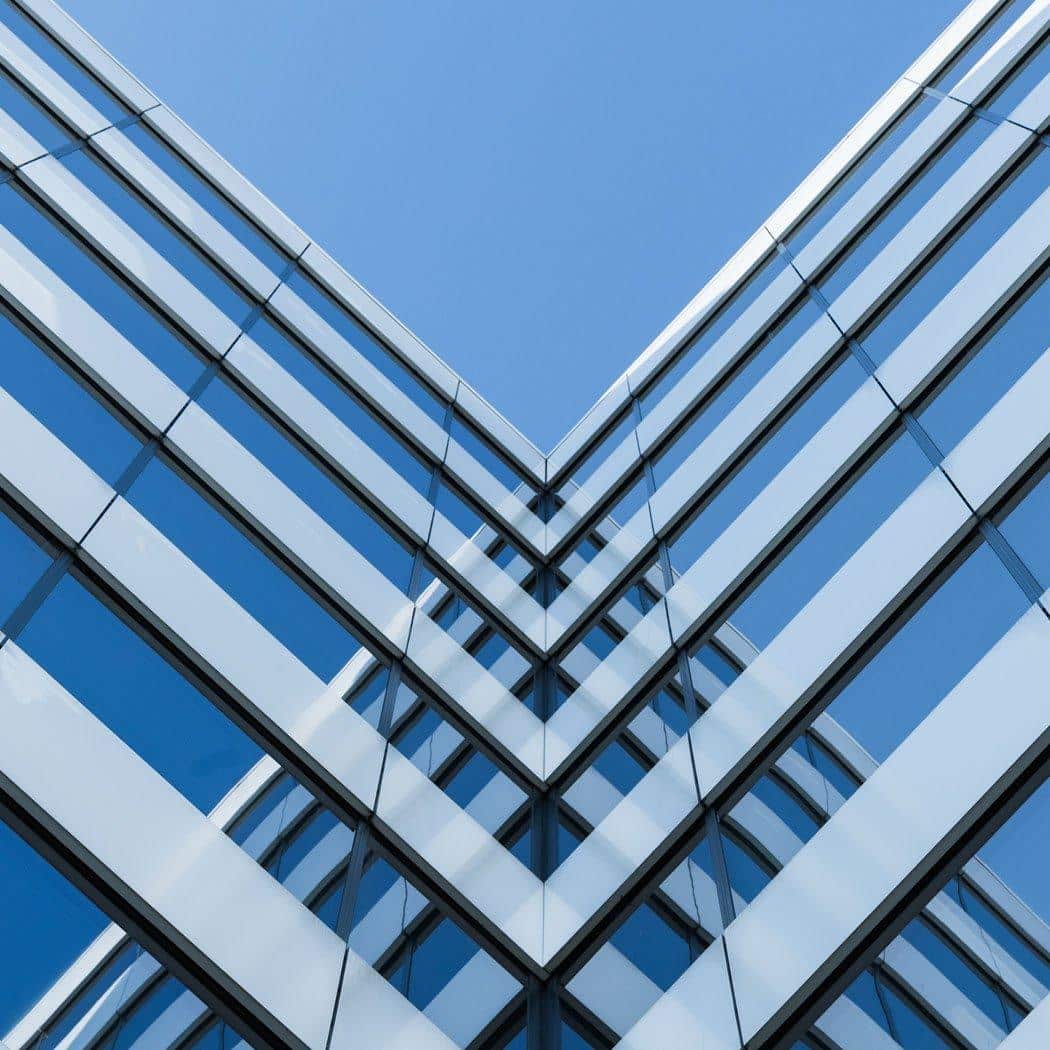 Upward view of intersecting glass office towers reflecting the sky, representing corporate structure, large-scale development, and complex financial transactions.
